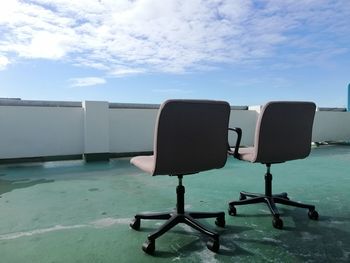 Empty chairs by swimming pool against sky