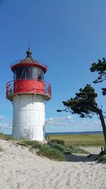 Lighthouse on beach against clear blue sky