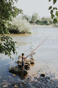 Shirtless boy fishing at river 