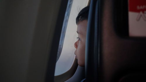 Close-up of man looking through airplane window