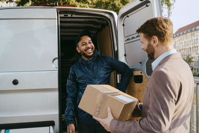 Mature man receiving parcel from male delivery person standing near van trunk