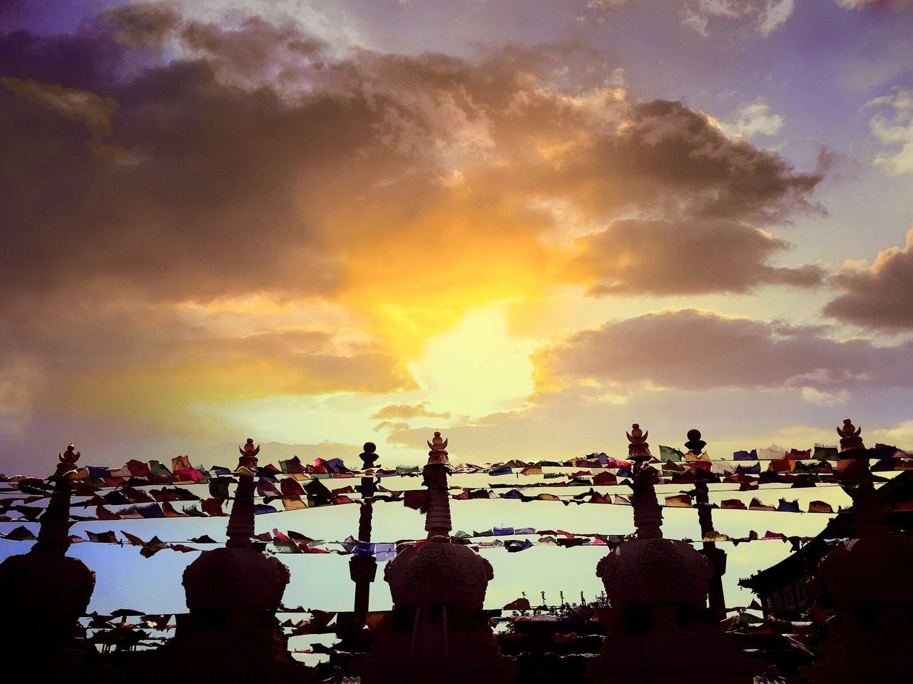 sky, sunset, cloud - sky, silhouette, sun, cloudy, cloud, built structure, nature, sunlight, outdoors, sea, low angle view, architecture, dusk, orange color, sunbeam, beauty in nature, no people, in a row