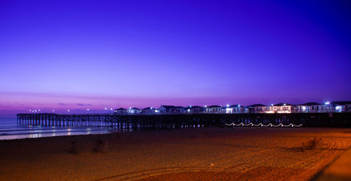 Illuminated buildings by sea against clear blue sky at night
