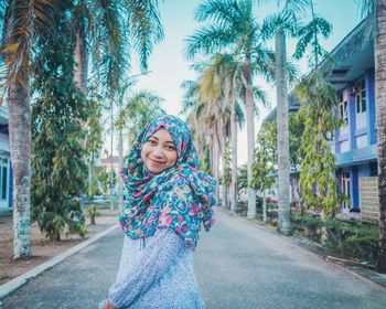 Portrait of smiling young woman standing on palm tree