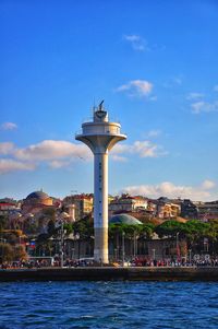 Tower in city at waterfront against cloudy sky