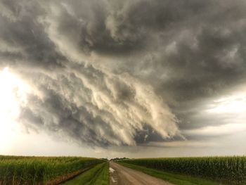 Road passing through field against cloudy sky