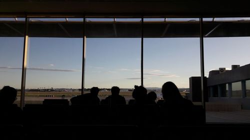 Silhouette people sitting by window against sky