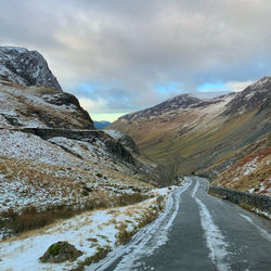 Road amidst snowcapped mountains against sky - honister mountain pass, lake district, cumbria