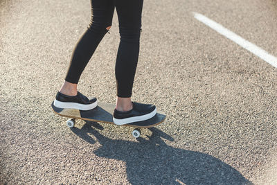 Low section of woman skateboarding on road