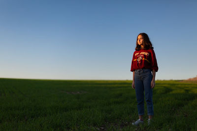Cute girl standing on grassy field against clear sky