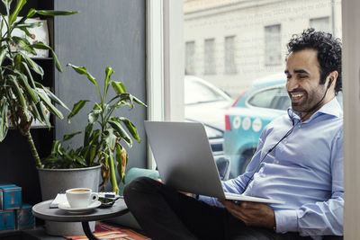 Happy businessman using laptop while sitting by window in creative office
