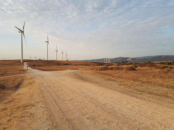 Road leading towards windmills against sky