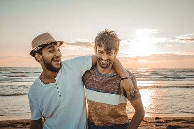 Happy friends standing on beach against sky