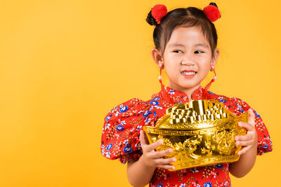 Portrait of young woman standing against yellow background