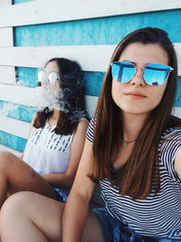 Portrait of smiling woman sitting with friend exhaling smoke