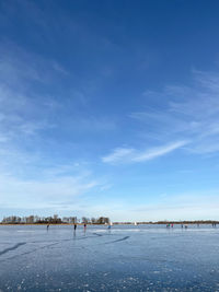 People walking on snow covered land against blue sky