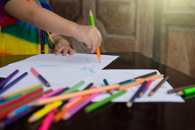 Midsection of woman holding multi colored pencils on table