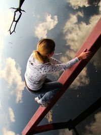 Low angle view of girl sitting on slide at playground against sky
