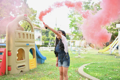 Happy girl holding distress flare while standing on grassy field at playground