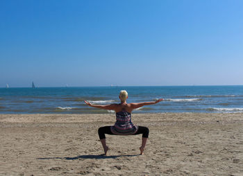 Woman doing yoga at beach against clear blue sky