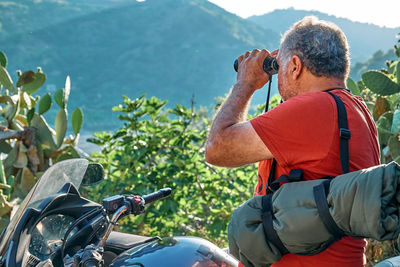 On the road.tourist man traveling on motorcycle,stopped for looking through binoculars at mountains 