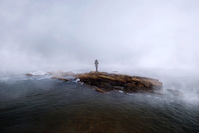 Person standing on rock in sea