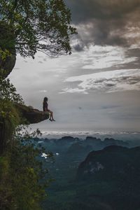 Man on cliff by sea against sky