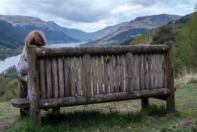 Rear view of woman sitting in on a bench looking at mountain and loch