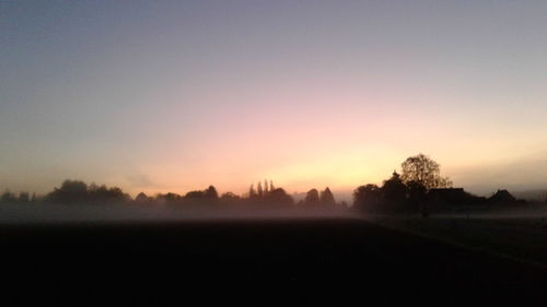 Silhouette trees on field against sky during sunset