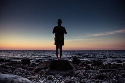 Full length of man exercising at beach against sky during sunset