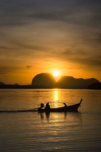 Silhouette people in sea against sky during sunset