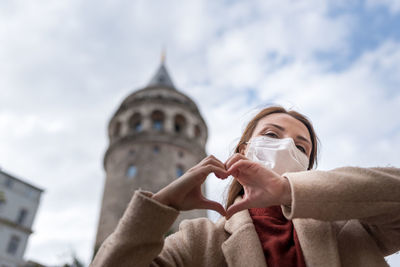 Low angle portrait of woman wearing mask standing against sky