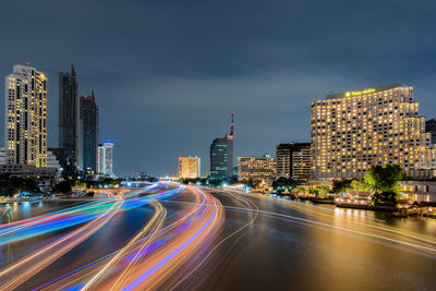 Light trails on road amidst buildings against sky at night