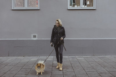 Full length of smiling woman standing with pomeranian dog on footpath against building