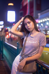 Beautiful young woman standing against illuminated lights at night