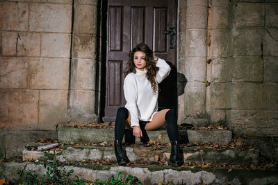 Full length portrait of woman sitting against wall