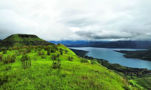 Scenic view of lush countryside and lake against cloudy sky