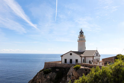 Lighthouse amidst buildings by sea against sky