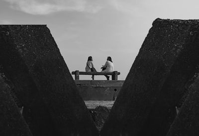 People sitting on retaining wall against sky