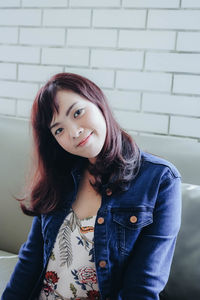 Portrait of smiling woman sitting on sofa against wall