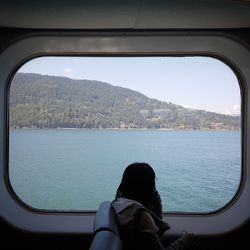 Rear view of woman looking at sea seen through window