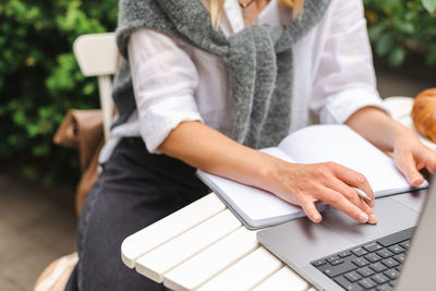 A woman takes notes in front of a laptop during an online business meeting outside.