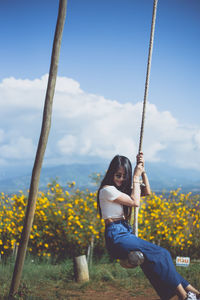 Woman sitting on swing against sky