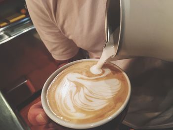 Cropped image of man pouring cream in coffee