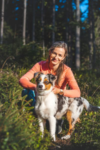 Portrait of young woman with dog standing in forest