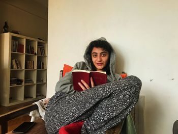 Portrait of young woman sitting on book at home