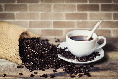 Close-up of coffee beans by cup on table against wall