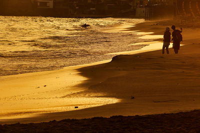 Silhouette friends taking selfie while standing at beach during sunset