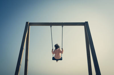 Rear view of girl swinging on swing at playground against clear sky