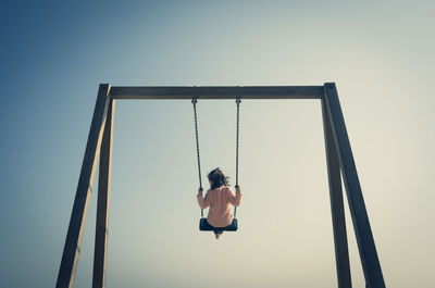 Low angle view of woman on swing at playground against sky